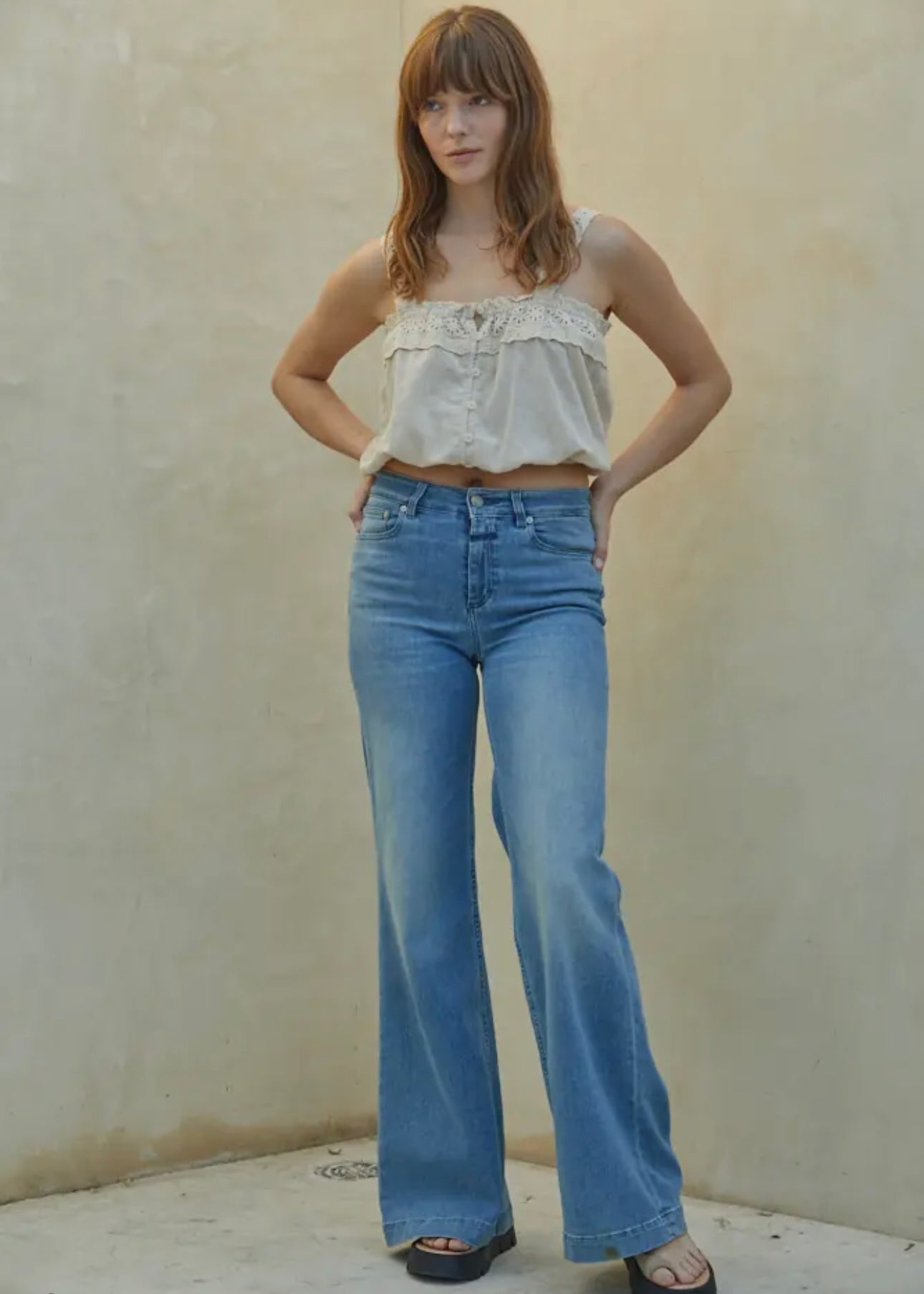Woman wearing a white top and blue jeans against a plain background